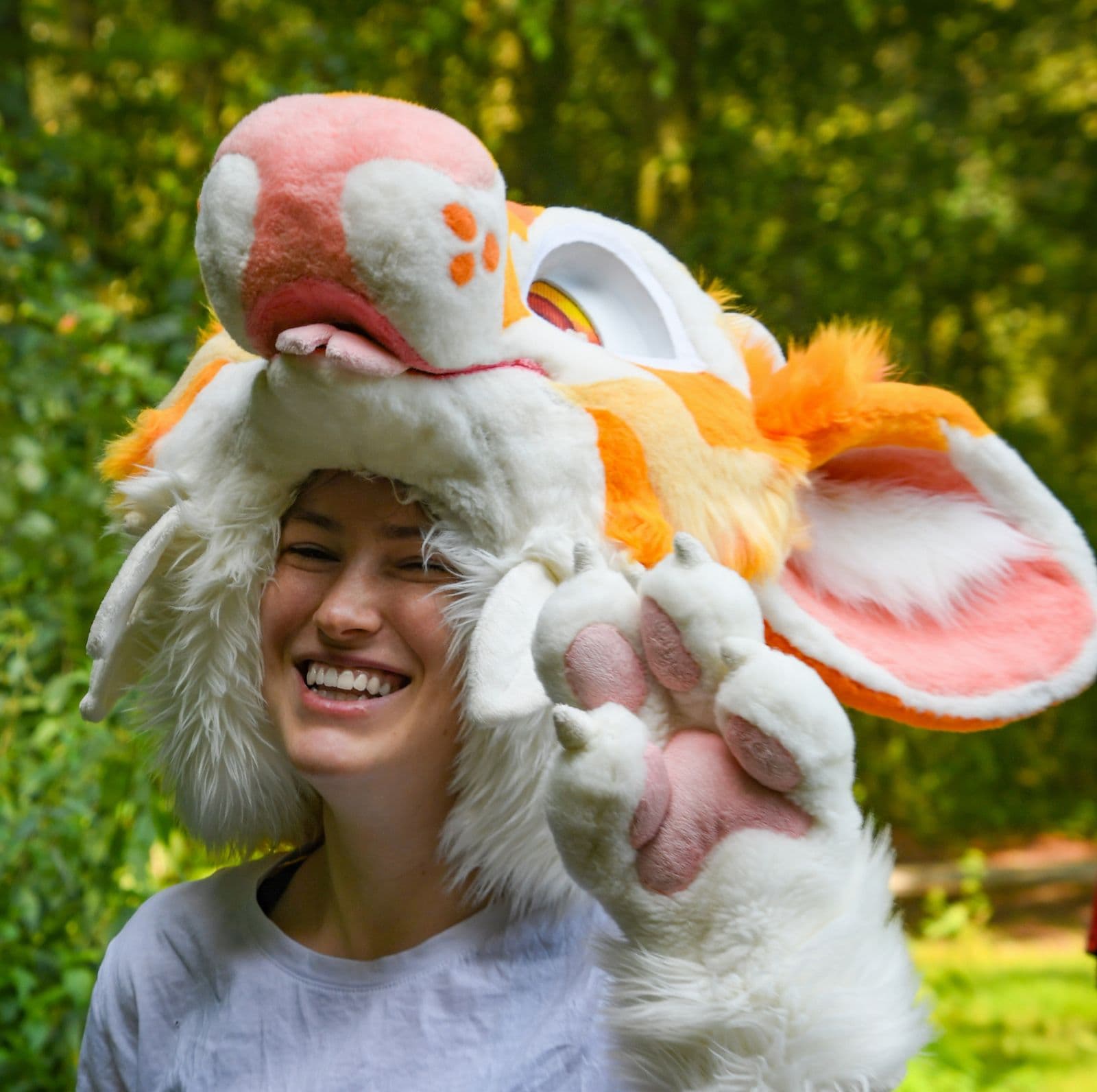 Chilli laughing with a fursuit head on, waving a paw at the camera